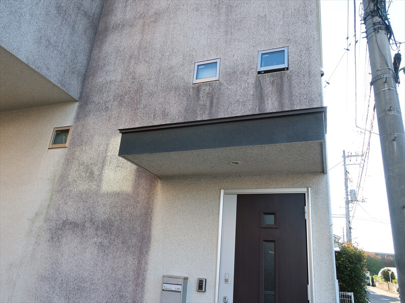 玄関等の屋根がある部分は元々の白い壁が見えていて、その他は黒く汚れています。